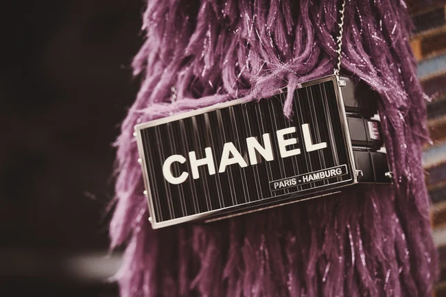 Ein Accessoire von Chanel vor einer Frau mit lila Kleid.